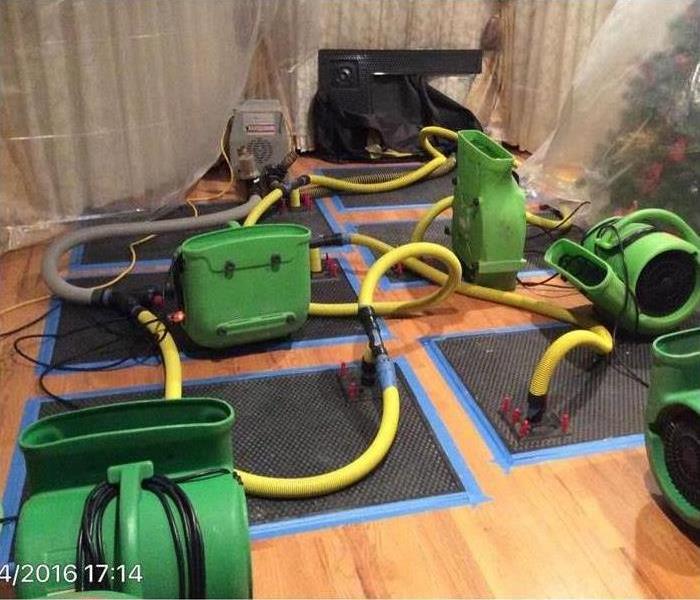 black drying mats, green air movers and plastic covers during drying service