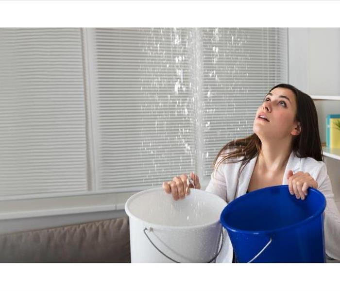 water pouring from living room ceiling into two bucket that woman is holding