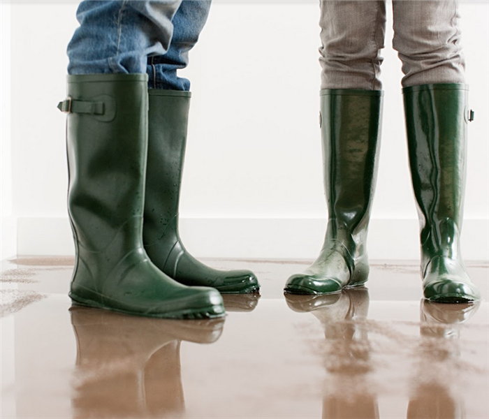 two people standing in water boots in a flooded room